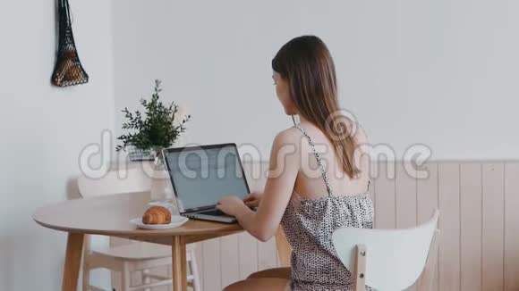 穿睡衣的女孩坐在桌子旁在笔记本电脑上打字穿着睡衣的苗条漂亮女人视频的预览图