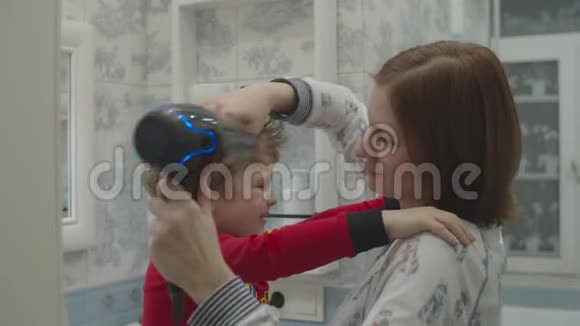 年轻的母亲用吹风机给儿子吹风一个穿着红色睡衣的孩子一边拥抱妈妈一边吹干头发家庭浴室视频的预览图