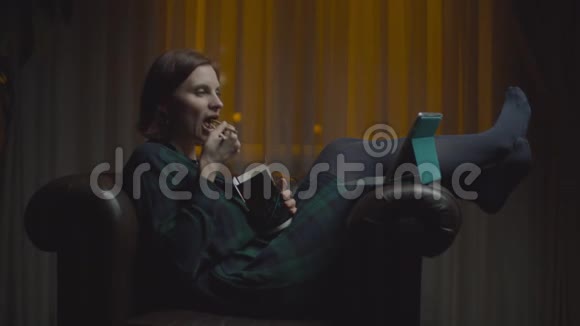 30多岁的女人在网上看平板电脑用筷子吃亚洲盒饭深夜坐在舒适的扶手椅上视频的预览图