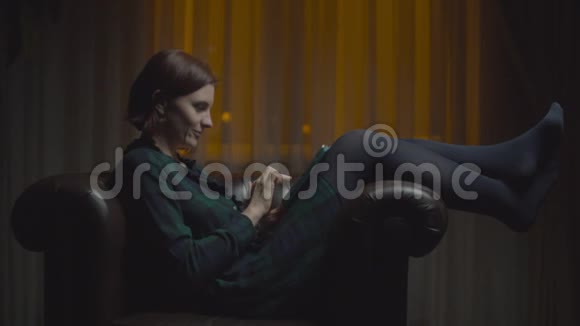30多岁的成年女性微笑着使用平板电脑打字很快深夜坐在舒适的扶手椅上放着路灯视频的预览图