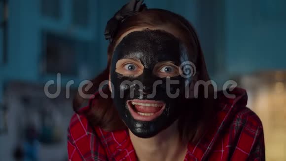 滑稽的30多岁的女人脸上戴着黑色的化妆面具在家里做鬼脸看着相机女人的脸很滑稽视频的预览图