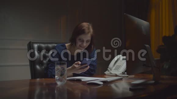 在夜店工作的年轻女商人女人笑着看着智能手机和显示器坐在一起视频的预览图
