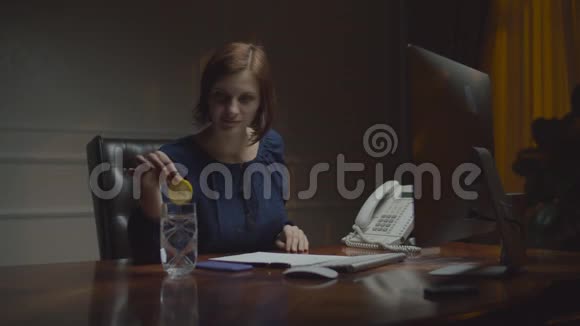 在夜间办公室工作的年轻女商人女人把平静的柠檬放进一杯水里喝工作视频的预览图