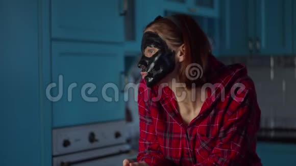滑稽的30多岁的女人脸上戴着黑色化妆面具在家里做鬼脸戴着蓝色面具做鬼脸的女人视频的预览图