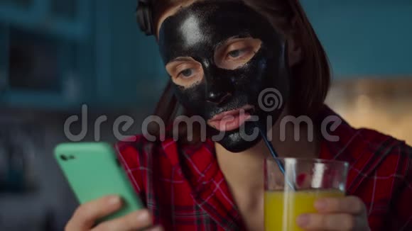 30多岁的年轻女性脸上戴着黑色化妆面具喝着一杯带有非塑料吸管的橙汁使用视频的预览图