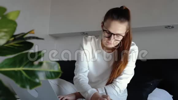 戴眼镜的年轻女子在家里用笔记本电脑在卧室里工作戴着面罩隔离和隔离是因为视频的预览图