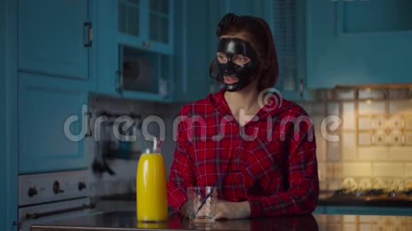 30岁的年轻女性脸上戴着黑色的化妆面具把橙汁倒进玻璃杯里喝不含酒精的饮料视频的预览图
