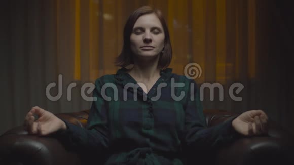 年轻的女性在莲花的位置冥想在舒适的扶手椅深夜女人在冥想时感到宁静视频的预览图