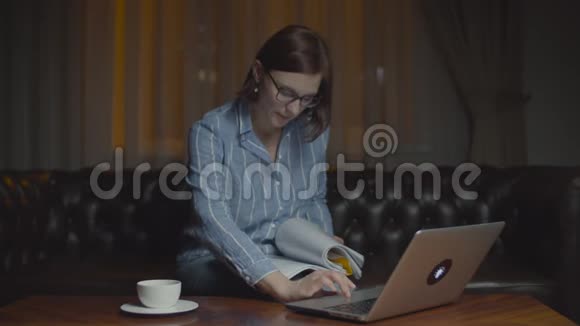 戴眼镜的年轻女商人晚上在家工作女人在看文件在笔记本电脑上打字视频的预览图