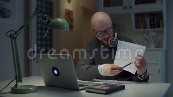 30多岁的留着胡子的戴眼镜的男人给在家里看笔记本电脑的学生展示一张有图表的纸在线教育视频的预览图