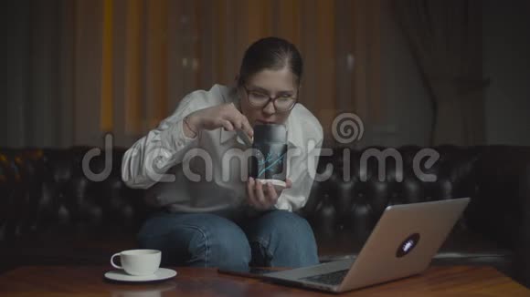 30多岁的女人戴着眼镜用筷子吃亚洲盒饭看着笔记本电脑显示器在沙发上吃晚寂寞的家宴视频的预览图