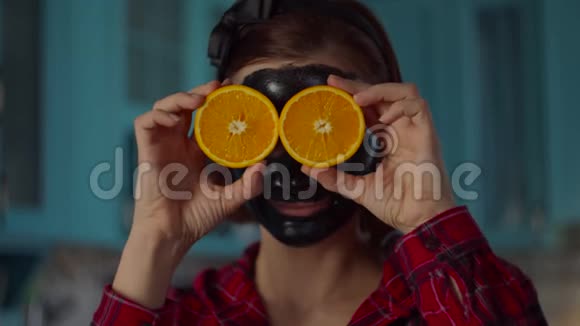 一个30多岁的女人脸上戴着黑色的化妆面具拿着橘黄色的水果两眼望着镜头女人视频的预览图