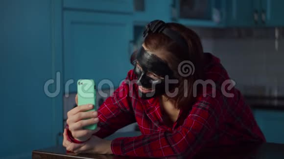30多岁的年轻女性使用手机在家里打视频电话脸上戴着黑色化妆面具女子美容常规视频的预览图