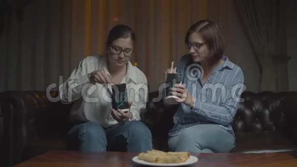 两个戴眼镜的女朋友用筷子吃亚洲盒饭女人会在深夜的沙发上搞笑聊天视频的预览图