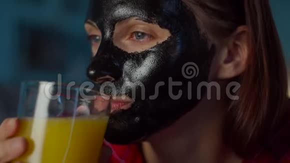 30多岁的年轻女性脸上戴着黑色化妆面具喝着一杯橙汁看着相机女人美丽视频的预览图