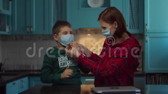 30岁的年轻母亲戴着医用口罩帮助孩子在家里戴着医用口罩戴医疗面具的家庭视频的预览图