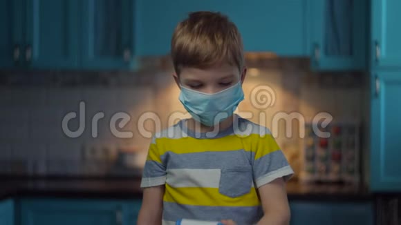 戴着医用面罩的金发男孩用红外温度计对着摄像机测量体温戴着医用口罩的孩子视频的预览图