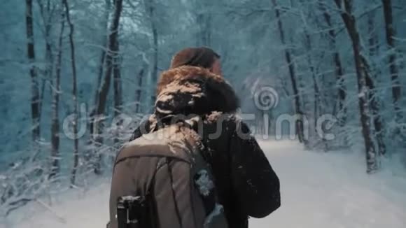 傍晚森林里雪花飘落的英俊的旅游背包客视频的预览图