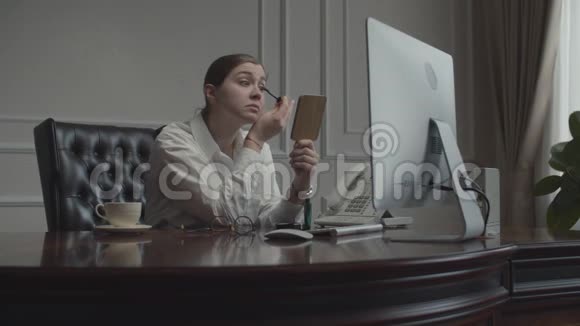 年轻的女商人在工作场所化妆照镜子女性坐在办公桌前电脑显示器在视频的预览图