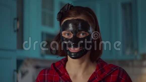 微笑的30多岁的女人脸上戴着黑色的化妆面具拿着猕猴桃半边靠近眼睛看着相机妇女视频的预览图