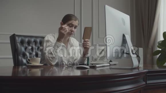 年轻的女商人在工作场所化妆照镜子女性坐在办公桌前带着监视器视频的预览图
