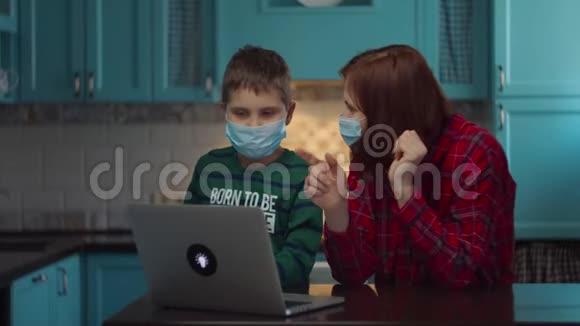 30岁的母亲和男孩戴着医用口罩看着手提电脑屏幕和亲戚们在网上聊天视频的预览图
