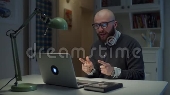 30多岁的大胡子戴眼镜的男人在家里打视频电话时在笔记本电脑上情绪化地交谈在线教育过程侧视视频的预览图