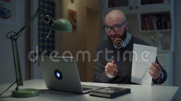 30多岁的留着胡子的戴眼镜的男人给在家里看笔记本电脑的学生展示一张有图表的纸在线教育视频的预览图