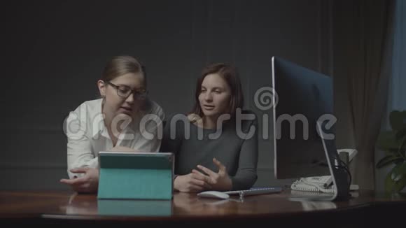 两个女商人晚上在办公室里用平板电脑工作女同事讨论工作问题视频的预览图