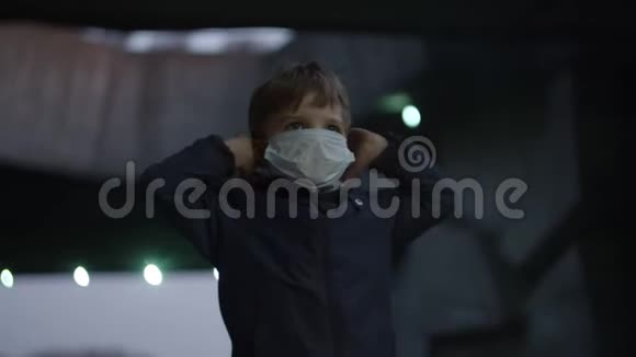 戴着医用防护面罩的男孩在大流行爆发冠状病毒COVID19时站在避难所里吓着手表视频的预览图