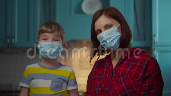 年轻的30岁的母亲和男孩戴着医疗面具看着相机家人在家里戴着医用口罩与家人隔离视频的预览图