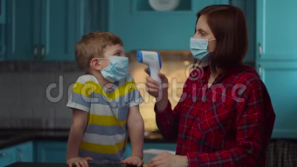 30岁的母亲戴着医用口罩用红外线温度计测量生病孩子的体温家里的家人视频的预览图