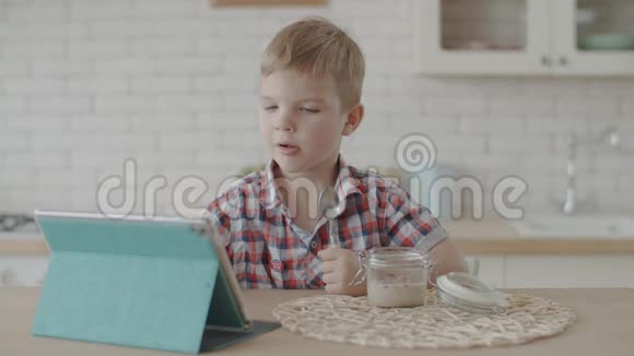 金发的蹒跚学步的男孩吃玉米片与纯素牛奶和喝苹果汁在白色厨房慢动作视频的预览图