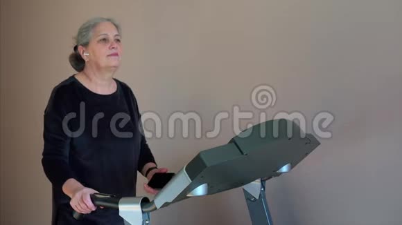 晨间工作时在跑步机上跑步的女人在她的智能手机上聊天视频的预览图