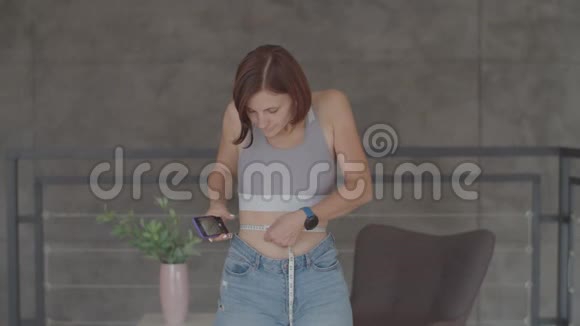 年轻女子在卧室里穿着旧牛仔裤欣赏减肥的结果微笑快乐的女性拍照视频的预览图
