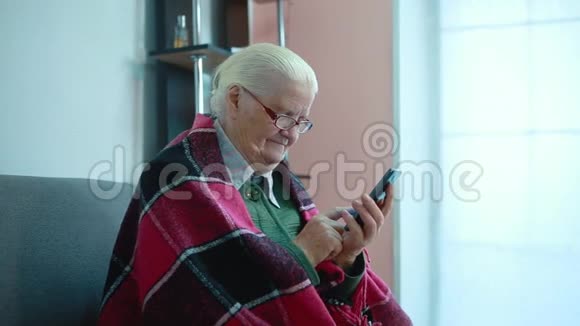 奶奶坐在智能手机的冲浪板沙发上视频的预览图