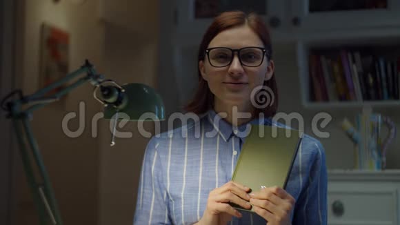 30多岁的女人戴着眼镜在家里拿着纸书和相机解释在线教育过程网络摄像机视图视频的预览图