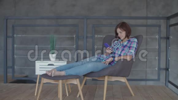 30多岁的黑发女子坐在扶手椅上在阁楼的室内公寓中缓慢地使用手机应用程序视频的预览图