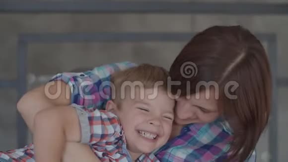 年轻的30多岁的黑发母亲和金发蹒跚学步的儿子坐在扶手椅上玩快乐的女人和男孩慢慢地笑视频的预览图