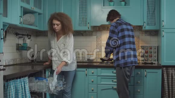 20多岁的年轻夫妇在家厨房卷发女人端盘子洗碗机男人煮早餐家庭视频的预览图