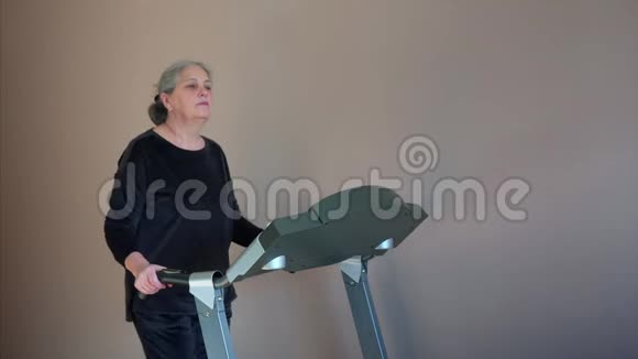老年妇女在家中跑步机上练习无线耳机视频的预览图