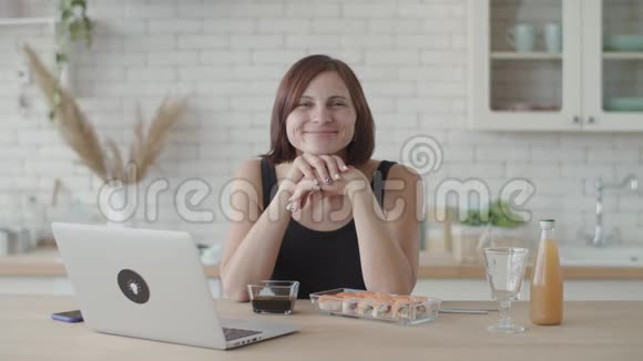 年轻的黑发女人穿着黑色连衣裙微笑着看着厨房桌子上的寿司相机欧洲女性视频的预览图