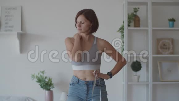 年轻女子在卧室里穿着旧牛仔裤欣赏减肥的结果微笑的女人测量她的腰视频的预览图