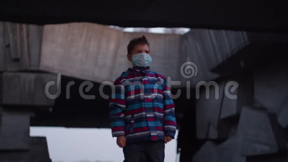 戴医用防护面罩的男孩在大流行爆发冠状病毒COVID19期间站在避难所并在周围观看视频的预览图