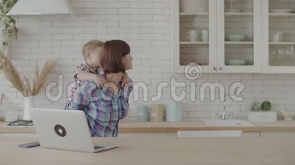 30多岁的年轻女子在白色的厨房里慢悠悠地和一个金发的蹒跚学步的男孩玩耍母子俩快乐视频的预览图