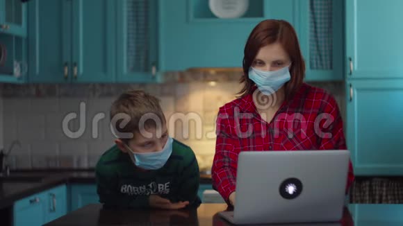 30岁的母亲和男孩戴着医用口罩看着手提电脑屏幕和亲戚们在网上聊天视频的预览图