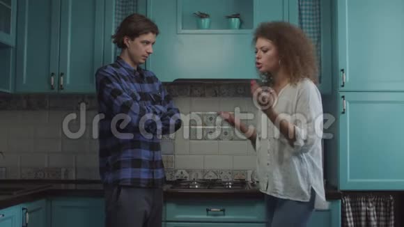 20多岁的年轻夫妇站在家里的蓝色厨房里吵架女友尖叫着指责男友家庭嫉妒视频的预览图