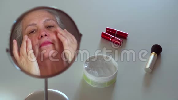 成熟的女人照镜子摸脸白色桌子上的化妆品视频的预览图