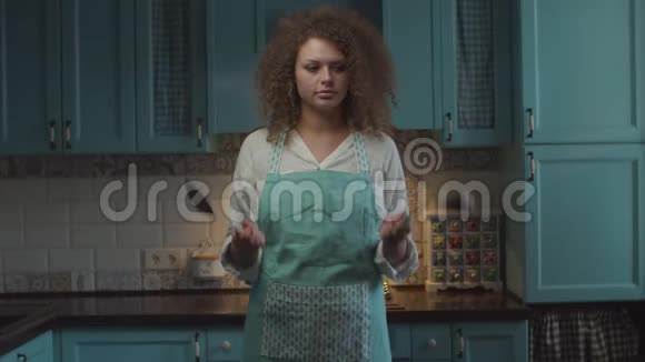 困惑的年轻卷发20多岁的妇女手里拿着厨房用具犹豫地摇头女人不知道怎么做视频的预览图