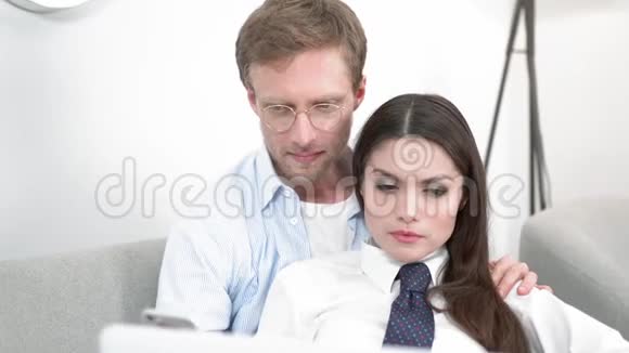 一个戴眼镜的年轻人拍照并分散他的妻子在笔记本电脑上工作视频的预览图
